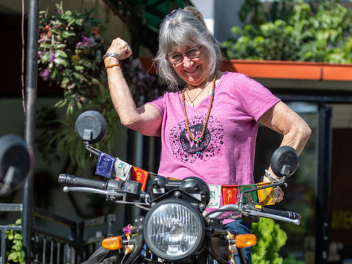 A woman standing on a bike smiling, one fist raised