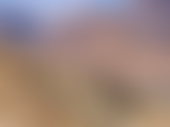 Motorcyclists stand on a rocky mountain path with three bikes. Majestic mountains and a valley village stretch under a sunny sky.