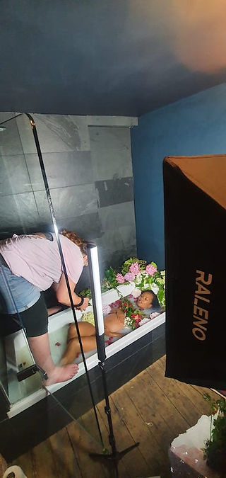Photographer HeardinLondon show a pregnant black woman a photograph of herself during a maternity photoshoot in a bath surrounded by flowers