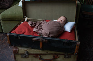 A baby is asleep in a green and brown vintage suitcase with orange lining.  The baby is wrapped in brown fabric and has a white pillow.  It is a landscape photograph.  It is a newborn baby portrait photograph taken by empowerment and confidence photographer HeardinLondon.