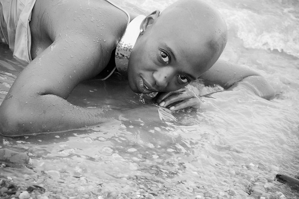 A monochrom photograph of a black woman with a shaved head lying on a beach.  It is an empowerment photograph by confidence photographer HeardinLondon