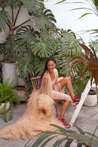 A woman in peach tulle sits in front of plants.   It is a portrait photograph taken by body confidence photographer HeardinLondon