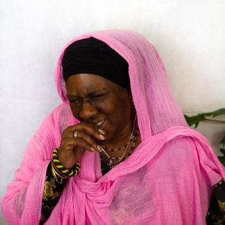 A black woman with a pink scarf and angold and black dress and looks at the camera. A portrait photograph by empowerment photographer HeardinLondon