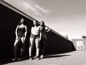 A black and white photograph of a group of teenagers in Hackney in front of wall.  It is a landscape photograph.  It is a coronavirus lockdown covid-19 doorstep portrait from empowerment photographer HeardinLondon.