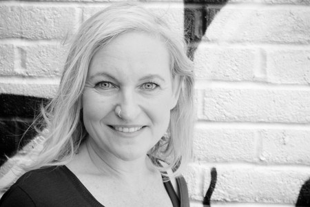 Black and white portrait photograph of a caucasian woman standing in front of brick wall