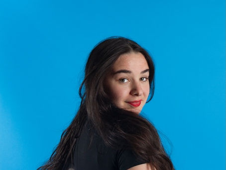 A caucasian woman with long brown hair stands in front of a blue backdrop. It is an empowerment photograph taken by confidence photographer HeardinLondon