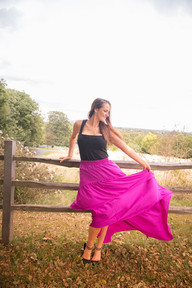 Caucasian woman in a pink skirt in a park leaning on a fence