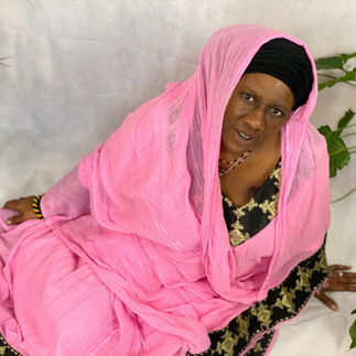 A black woman with a pink scarf and angold and black dress and looks at the camera. A portrait photograph by empowerment photographer HeardinLondon