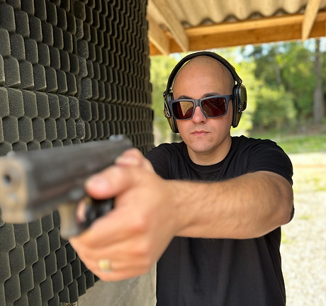 Foto do instrutor de tiro Alisson da Costa em um estande de tiro aberto, segurando uma pistola na mão