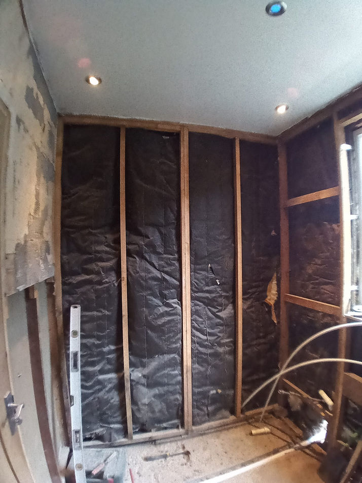Interior wall construction with wooden frame, black insulation, and ceiling lights.