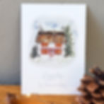Das Bild zeigt eine A6-Weihnachtskarte. Darauf ist ein weißes Cottage und Strohdach mit Tannenbäumen, Schnee und Weihnachtsdekoration.