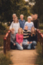 Familieportræt med flere generationer samlet udendørs på bro i grønne omgivelser