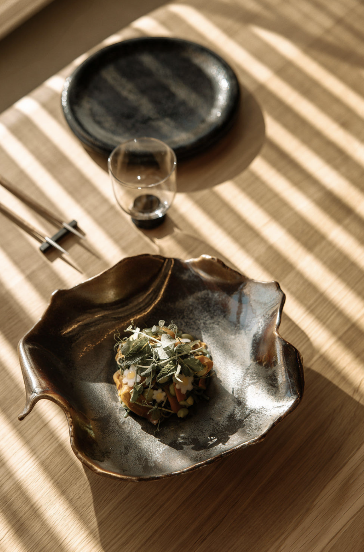 Gourmet dish in a unique plate with chopsticks and glass on the table.