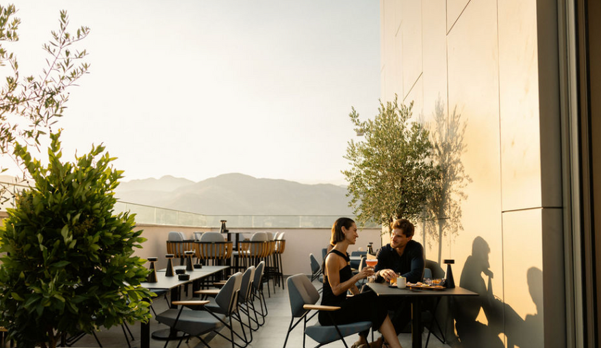 Couple enjoying drinks outdoors at a restaurant, mountains in the distance.
