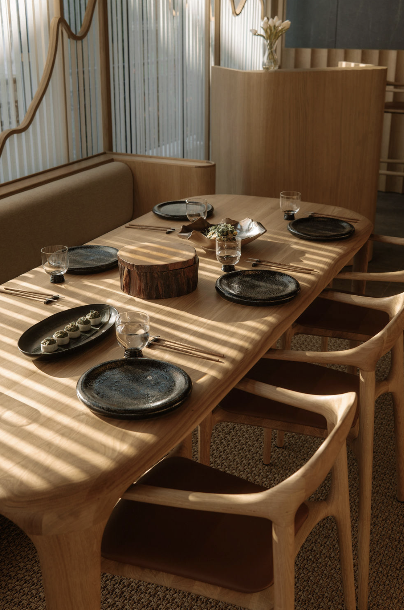 Wooden dining table set with plates, glasses, and chairs, restaurant indoor setting.