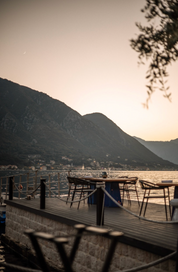 Wooden deck with chairs, mountains, and water view at sunset.