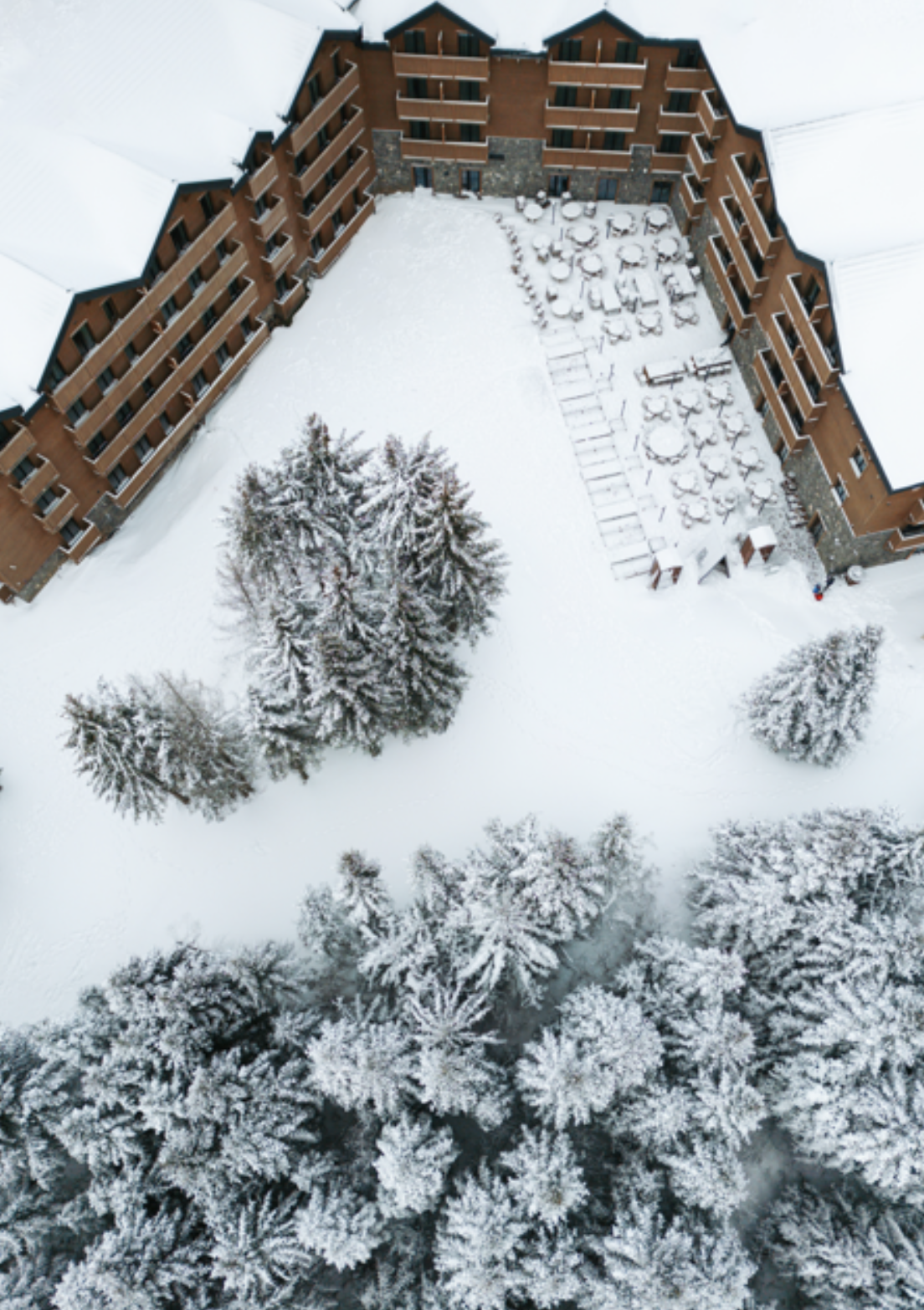 Aerial view of a snow-covered hotel surrounded by evergreen trees in winter