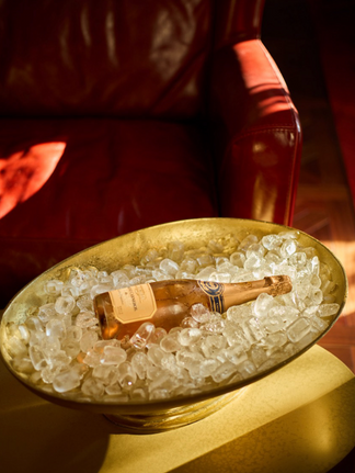 Champagne bottle in ice bucket next to a red leather chair.