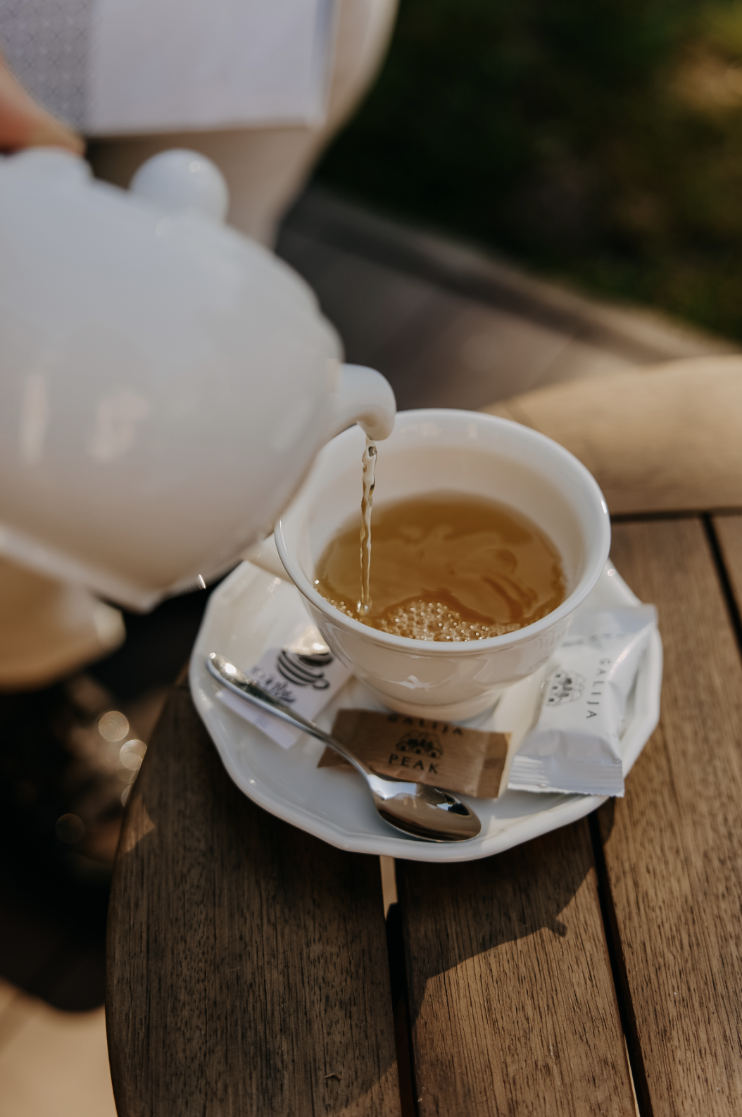 White teapot pouring tea into a white teacup on a wooden table.