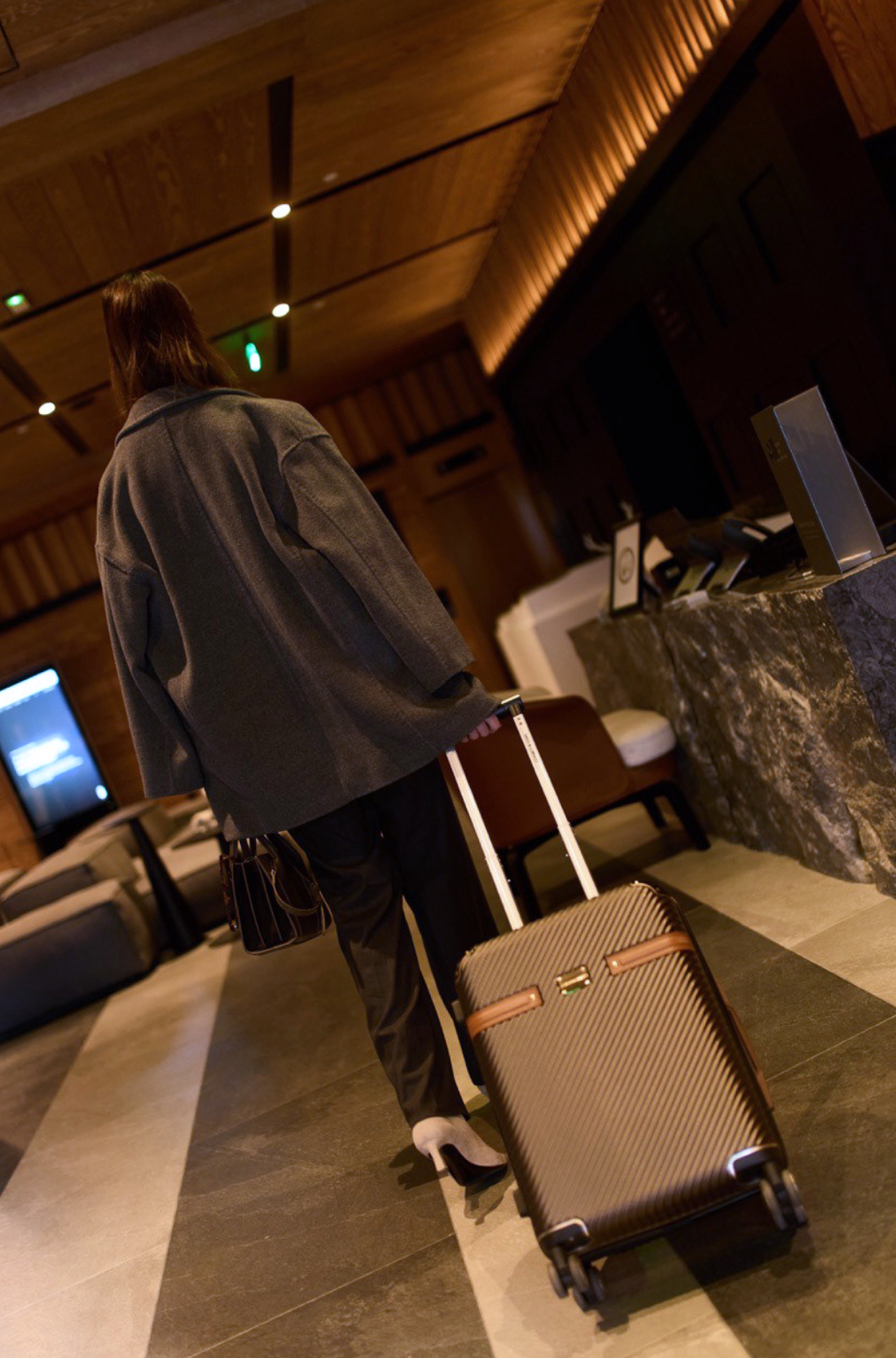Person walking with luggage at a hotel check-in desk, hotel interior background.