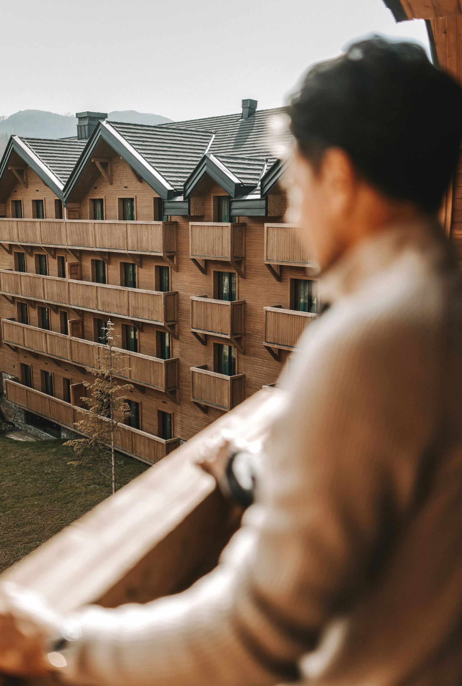 Man overlooking a wooden resort with mountain views and a sunny day.