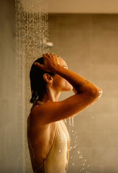 Woman enjoying shower, water cascading from above, wet hair, relaxing, indoor setting.