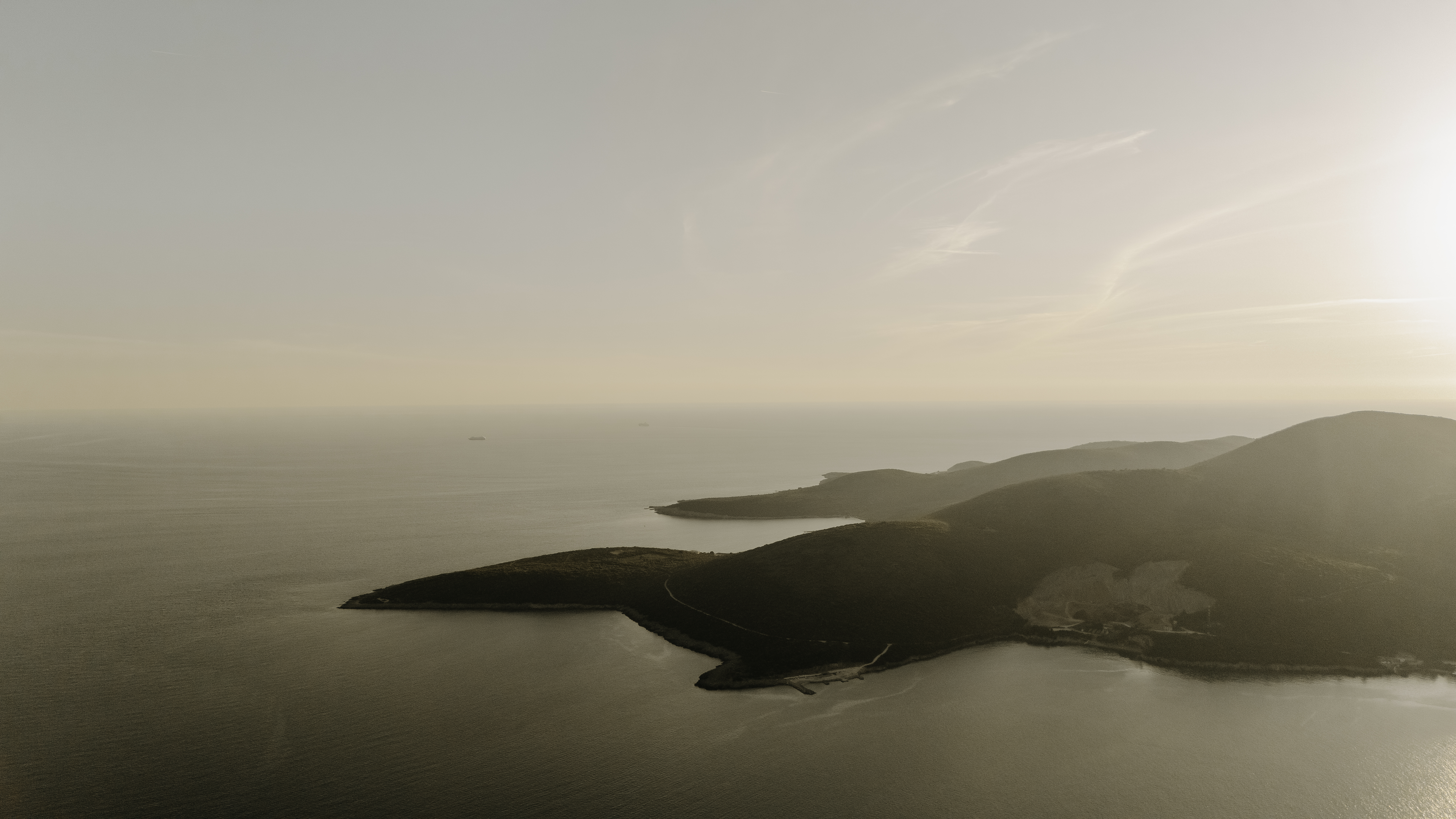 Aerial view of a coastal landscape with calm sea and hills in the sunlight.