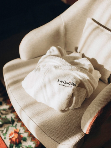 White bathrobe on armchair with Swissotel logo; relaxing hotel room scene