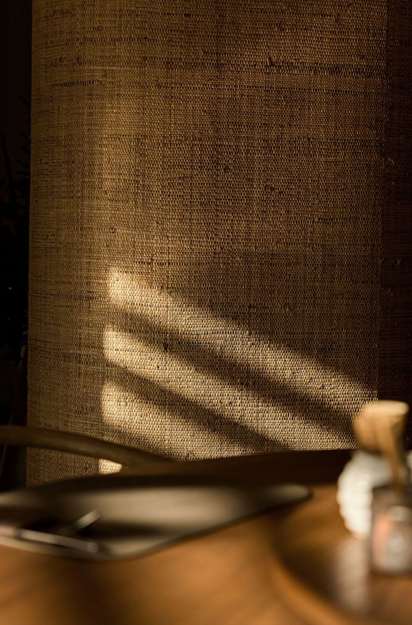 A lamp casts shadows and light on a brown woven wall