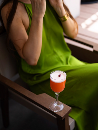 Woman in green dress holds cocktail glass, enjoying the drink, relaxed style