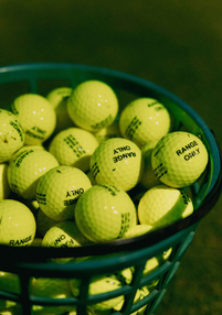Green basket filled with yellow golf balls labelled "RANGE ONLY".