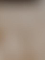 White teacup with tea sits on a white saucer on a bed.