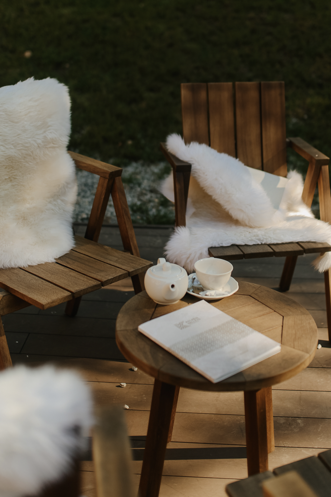 Wooden chairs with sheepskin and table with tea set outside in the sunlight.