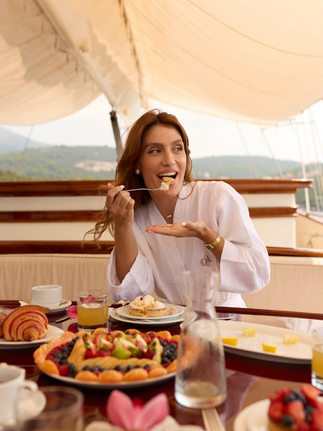 Woman enjoying breakfast on Riana Yacht, smiling with food, sunny day setting.