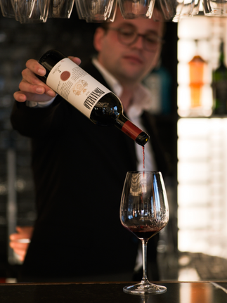 Bartender pours red wine into a glass. Wine bottle and label are visible.