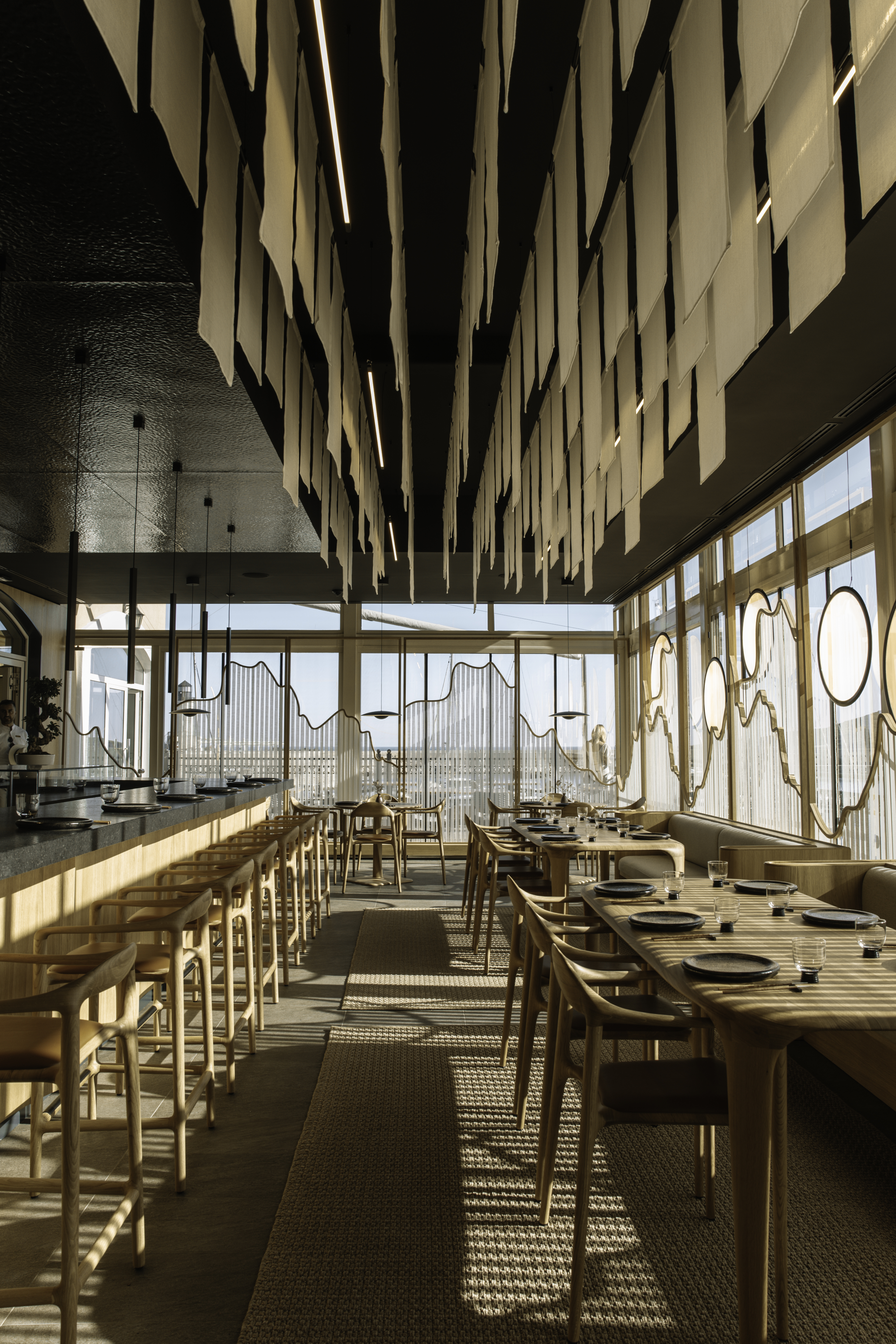 Elegant restaurant interior with long tables, bar, and artistic ceiling decor and mountain view.