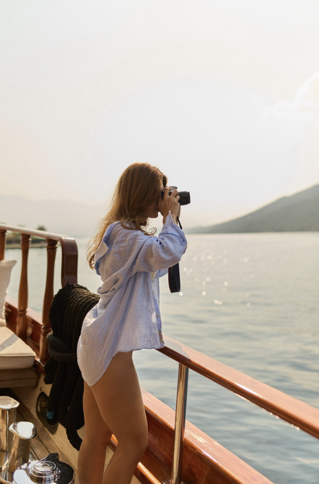 Woman taking a photo on a boat, sea and mountains in the background.