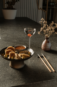 Dumplings with sauce, cocktail, and chopsticks on a table setting.