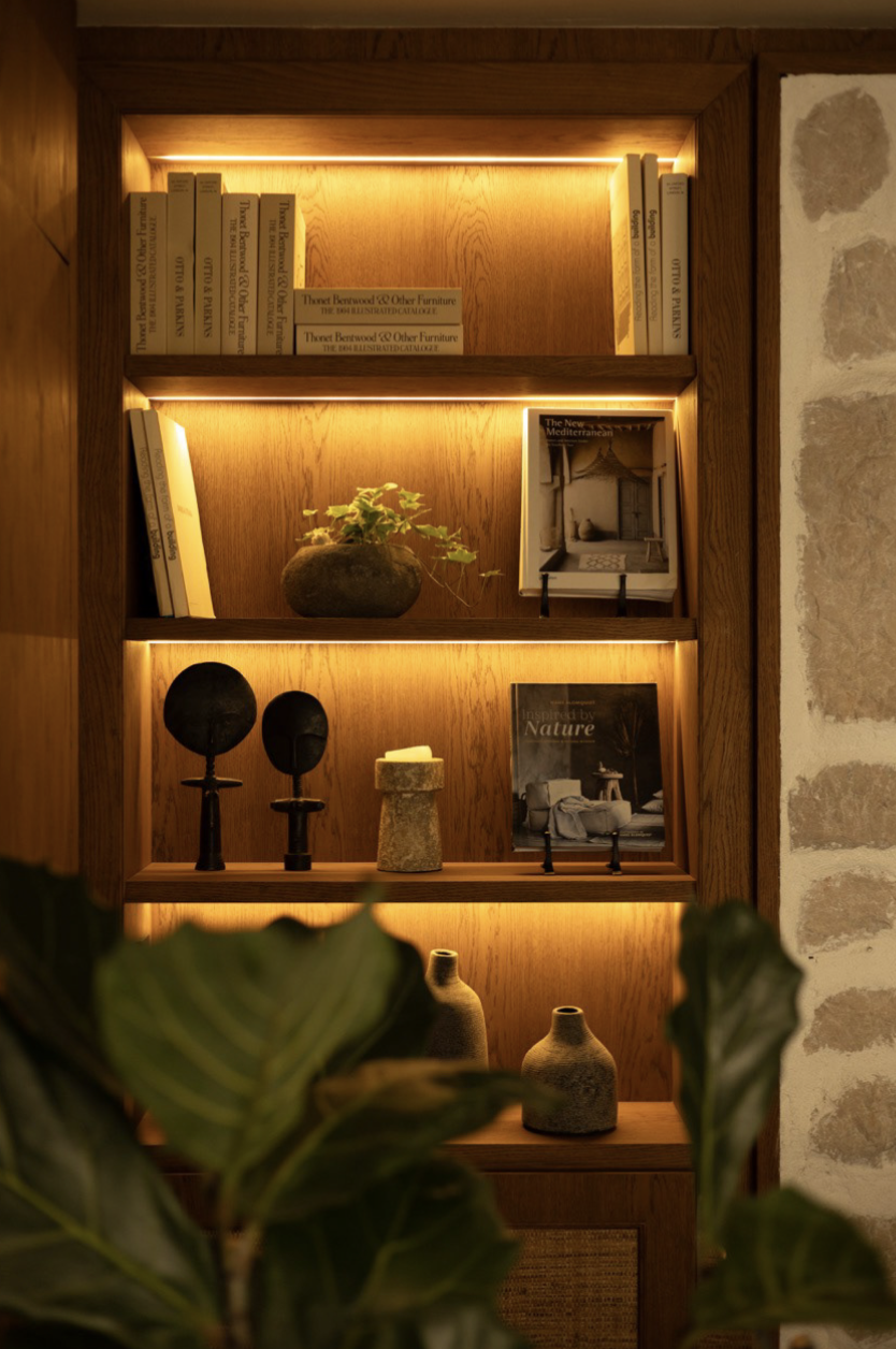 Wooden bookshelf with books, art, and decor illuminated by warm lighting.