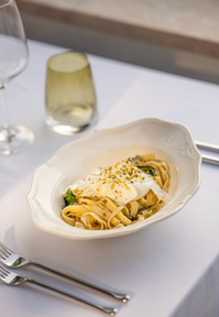 Pasta dish with egg and garnish on a white plate and tablecloth.
