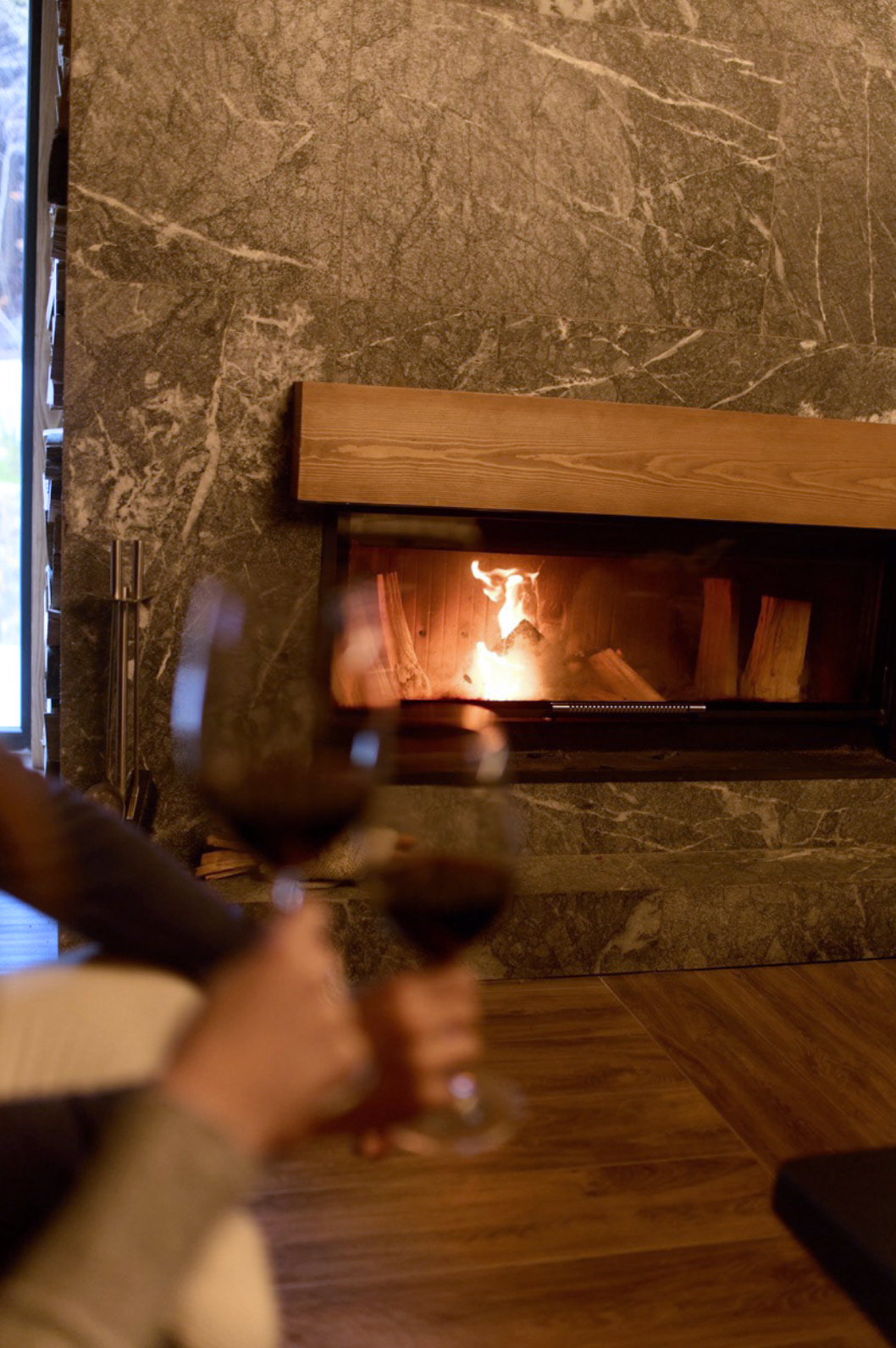 Two wine glasses clink in front of a cozy fireplace scene home.