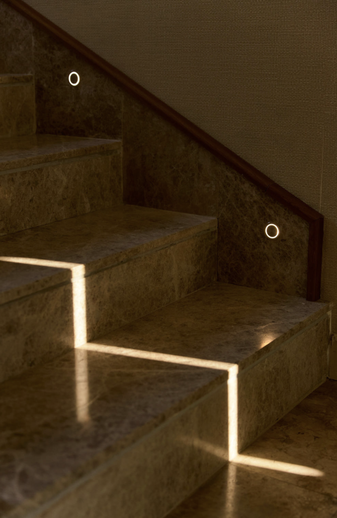 Illuminated staircase with lights, wooden handrail, and marble steps, home interior design.