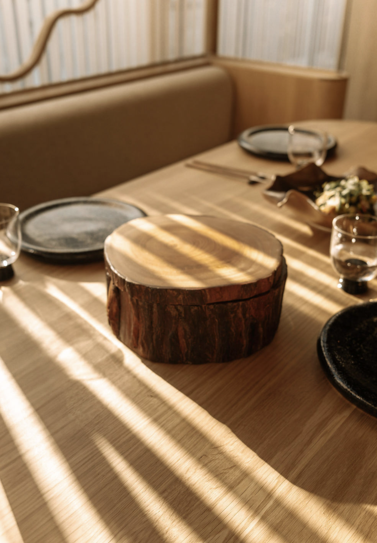 Wooden box on table with sunlight shadows; restaurant interior, food close by.