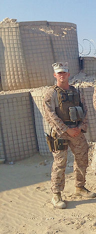 USMC veteran, Dr. Kristopher Biegel, owner of NexusLetterNow, standing in the desert with sand barriers in the background, while deployed overseas.