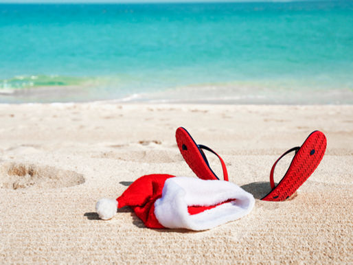 A tropical beach scene with a red Santa hat resting on a sun lounger, combining summer and Christmas imagery to reflect the concept of writing holiday songs out of season.