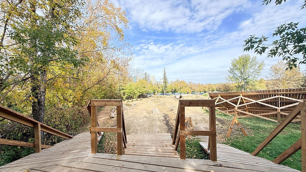 A timber start platform with handrails and three lanes dropping toward a dirt jump area, under a blue sky with fall trees.