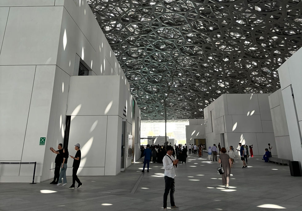 Courtyard of the Louvre Abu Dhabi with its distinctive perforated dome roof. Sunlight streams through the geometric pattern, casting spots of light on the floor. Visitors stroll and stand calmly in the space. Private photo taken in front of modern architecture.
