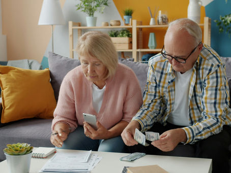 Elderly couple on a sofa counting cash and checking a phone amid bills in a cozy living room, looking focused and worried. How Much money retirees need to save for retirement?