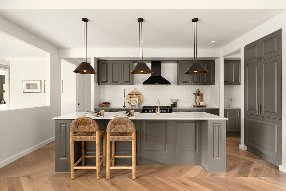 Modern kitchen with gray cabinets, white island, wicker stools, and three black pendant lights over herringbone wood floor.