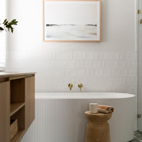 Freestanding fluted bathtub with patterened floor tiles and timber stool next to bath.